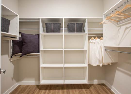 a walk in closet with white shelving and pillows