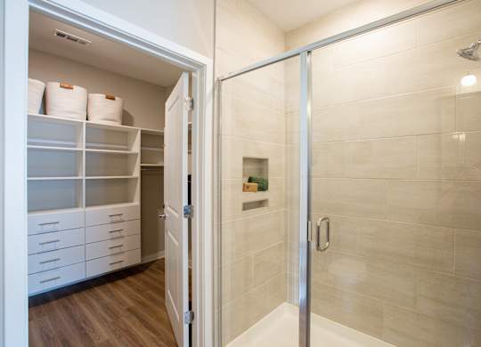 a walk in shower with a glass door and a closet with white shelves