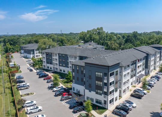 an aerial view of a large apartment complex with a parking lot and trees in the background