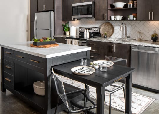 a kitchen with dark cabinets and a large island with a black table and two chairs