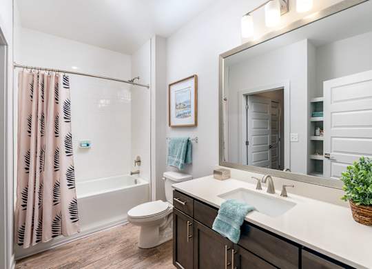 A bathroom with a white sink, toilet, and a shower with a pink shower curtain.