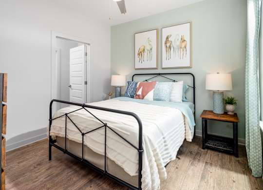 A bedroom with a black metal frame bed, a white comforter, and a small wooden table with a lamp on it.