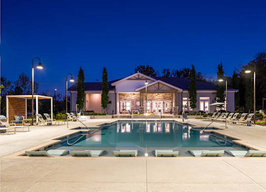 A large swimming pool in front of a building with lounge chairs around it.
