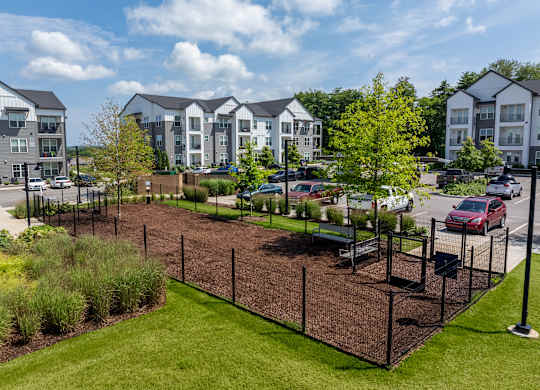 A view of a landscaped area with a fence and apartment buildings in the background.