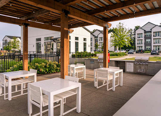 A patio with white chairs and tables under a wooden pergola.