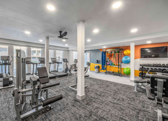 a gym with exercise equipment and a tv in a building with windows