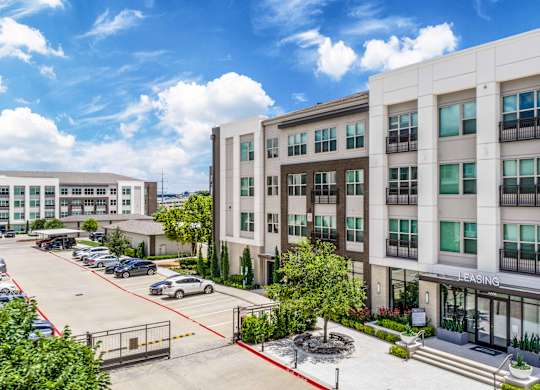 A parking lot in front of a multi-story building with a sign that says "Leasing.".