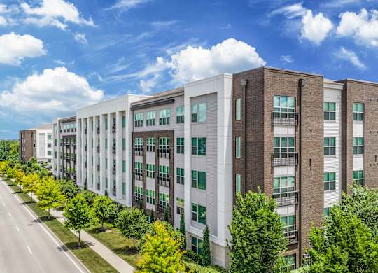 A row of modern apartment buildings with trees lining the street.