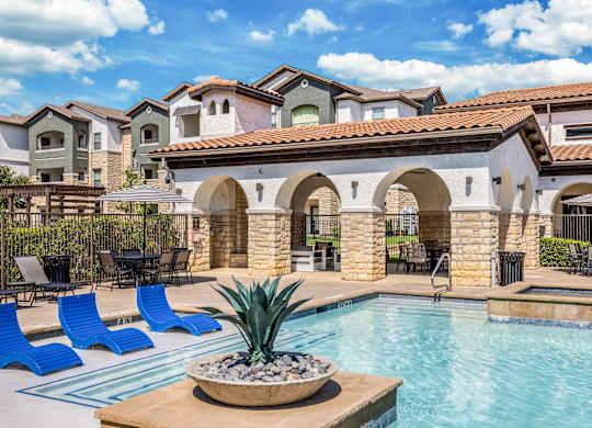A pool area with a stone archway and blue lounge chairs.