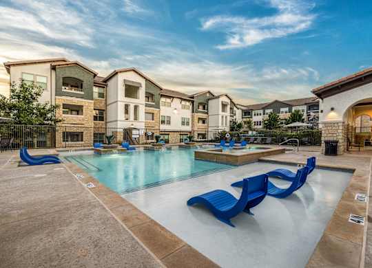 A swimming pool with blue loungers in front of apartment buildings.