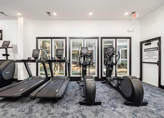 A gym with treadmills, elliptical machines, and a warning sign.