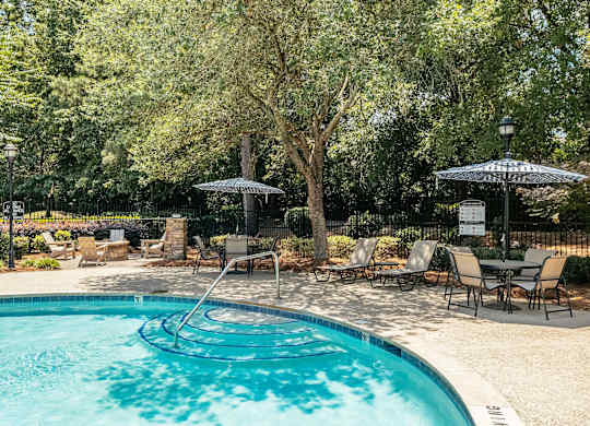 A pool surrounded by trees and chairs.