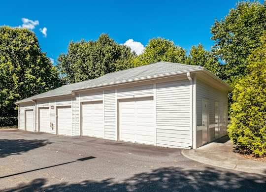 A two-car garage with a grey roof and white walls is surrounded by greenery.