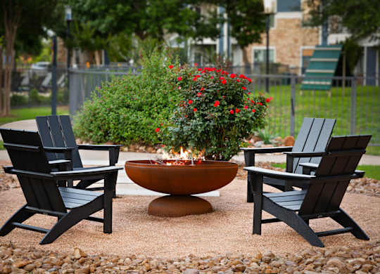 A fire pit surrounded by two chairs and a planter with red flowers.