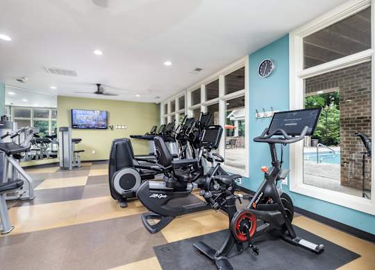 A gym with a row of stationary bikes and a television mounted on the wall.