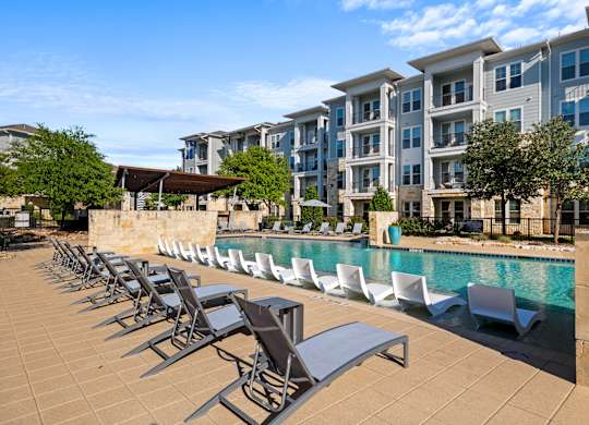 A pool area with sun loungers and a building in the background.