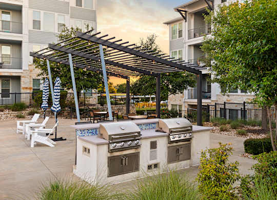 A patio with a grill and chairs under a pergola.