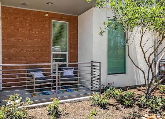 A small patio with a bench and a tree in front of a white house.