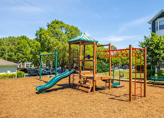 A playground with a green slide and a red swing set.