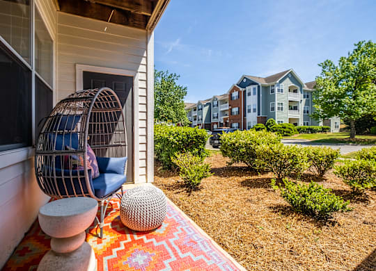 A patio with a chair and a table is in front of a house.
