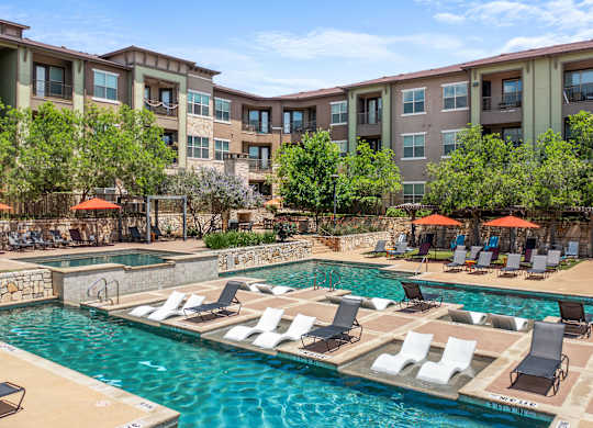 A large swimming pool with lounge chairs and umbrellas in front of apartment buildings.