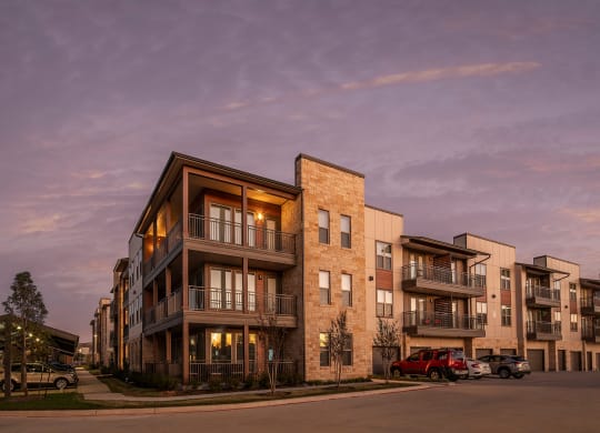 a rendering of a building at dusk with the lights on and cars parked in front of it