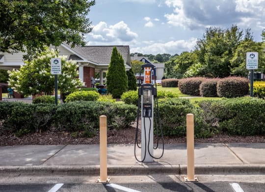 a gas pump in a parking lot with a house in the background