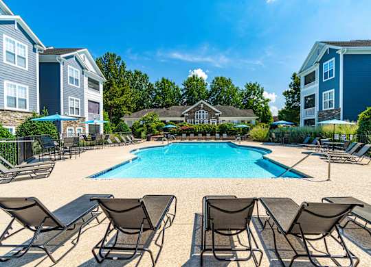 A swimming pool surrounded by lounge chairs and umbrellas in a residential area.