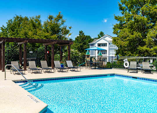 A pool with a wooden pergola and lounge chairs.