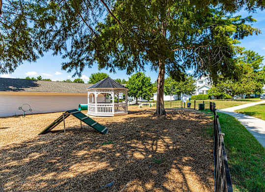 A playground with a green slide and a white gazebo.