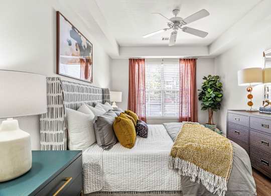 A bedroom with a bed, a ceiling fan, and a nightstand with a lamp.