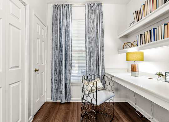 A room with a chair, a desk, and a window with curtains.