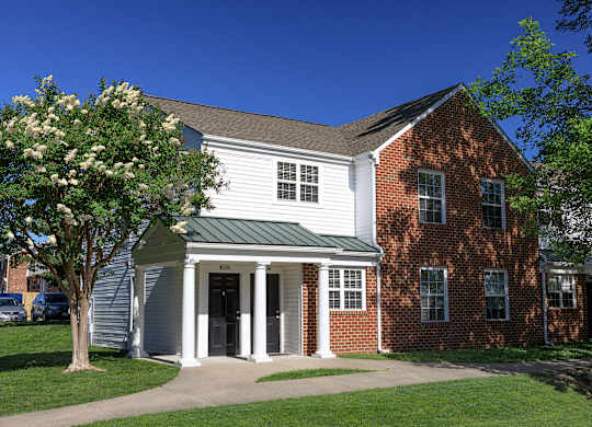 A white building with a green roof and a tree in front.