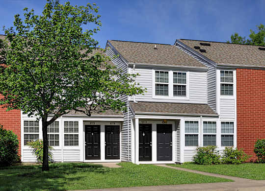 A white house with a black door and a tree in front.
