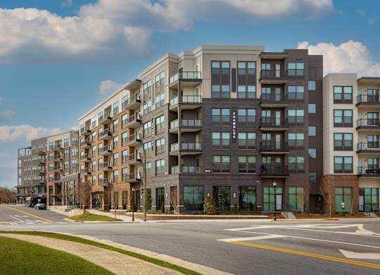 A row of modern apartment buildings line a tree-lined street.