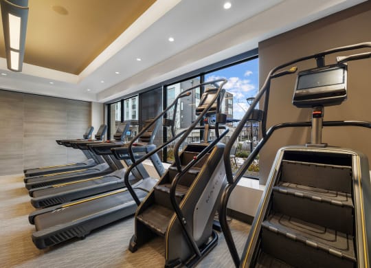 a gym with cardio equipment and a row of windows