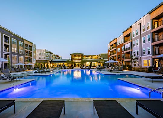 a large swimming pool with lounge chairs and umbrellas in front of a building