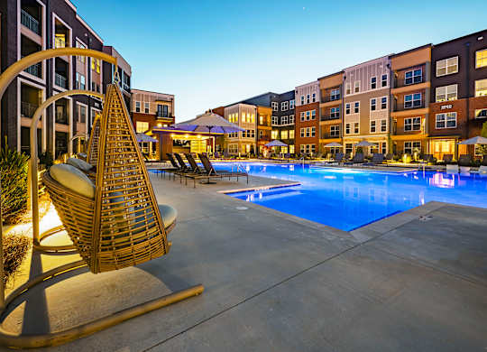 a swimming pool with lounge chairs and umbrellas in front of an apartment building