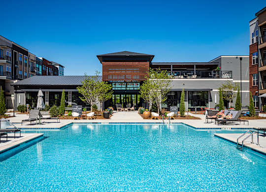 a large pool with lounge chairs and umbrellas in front of a building
