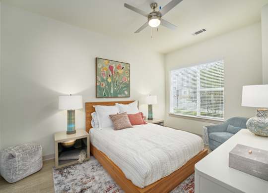 A bedroom with a large bed, a ceiling fan, and a painting on the wall.