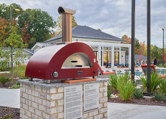 A red pizza oven sitting on a brick base with a sign in front of it.