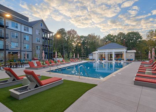 A swimming pool surrounded by red lounge chairs and a gazebo.