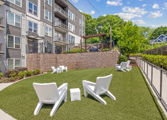 A row of white chairs are set up on a green lawn.