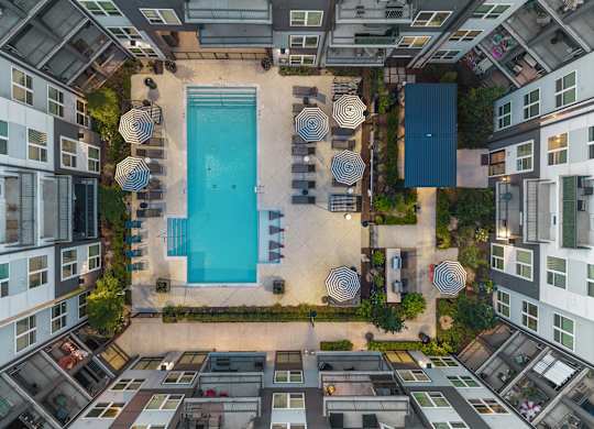 A swimming pool surrounded by lounge chairs and umbrellas in a courtyard.
