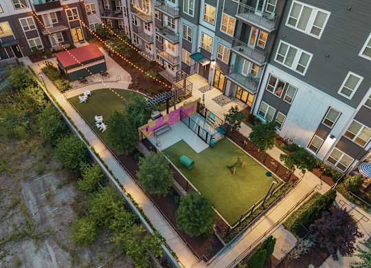 A small park with a playground and a green lawn is surrounded by apartment buildings.
