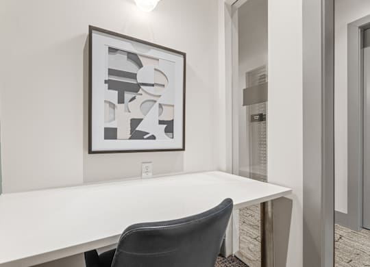 A white desk with a black chair and a framed artwork on the wall.