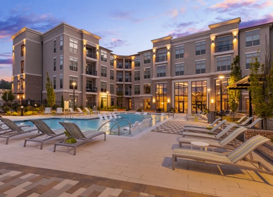a large swimming pool with chaise lounge chairs and a building in the background