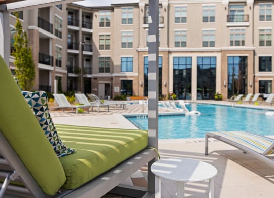 a pool with lounge chairs and a coffee table in front of an apartment building