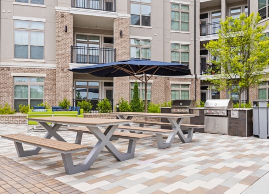 two picnic tables with umbrellas in front of an apartment building