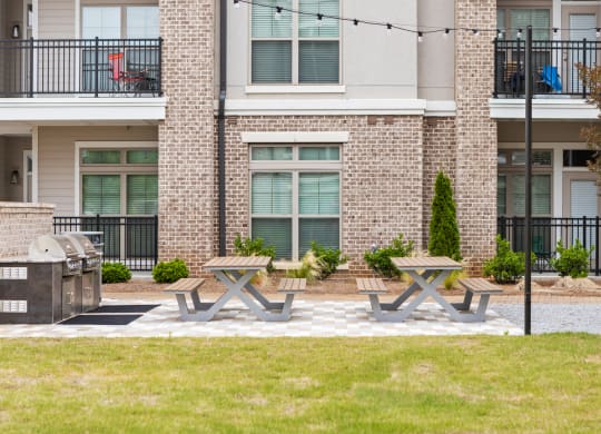 a picnic area with two picnic tables and a grill in front of an apartment building